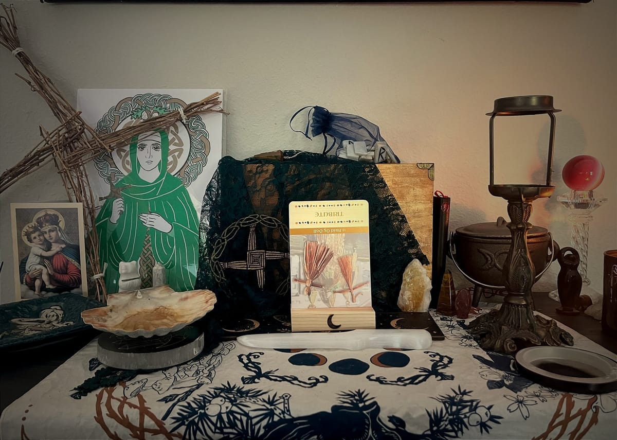 A photo of an altar containing photos of St. Brigid, a veil, runes, various crystals and an oracle card in reverse.