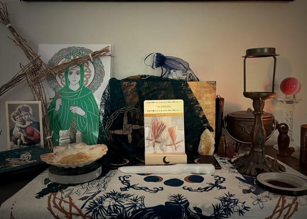 A photo of an altar containing photos of St. Brigid, a veil, runes, various crystals and an oracle card in reverse.